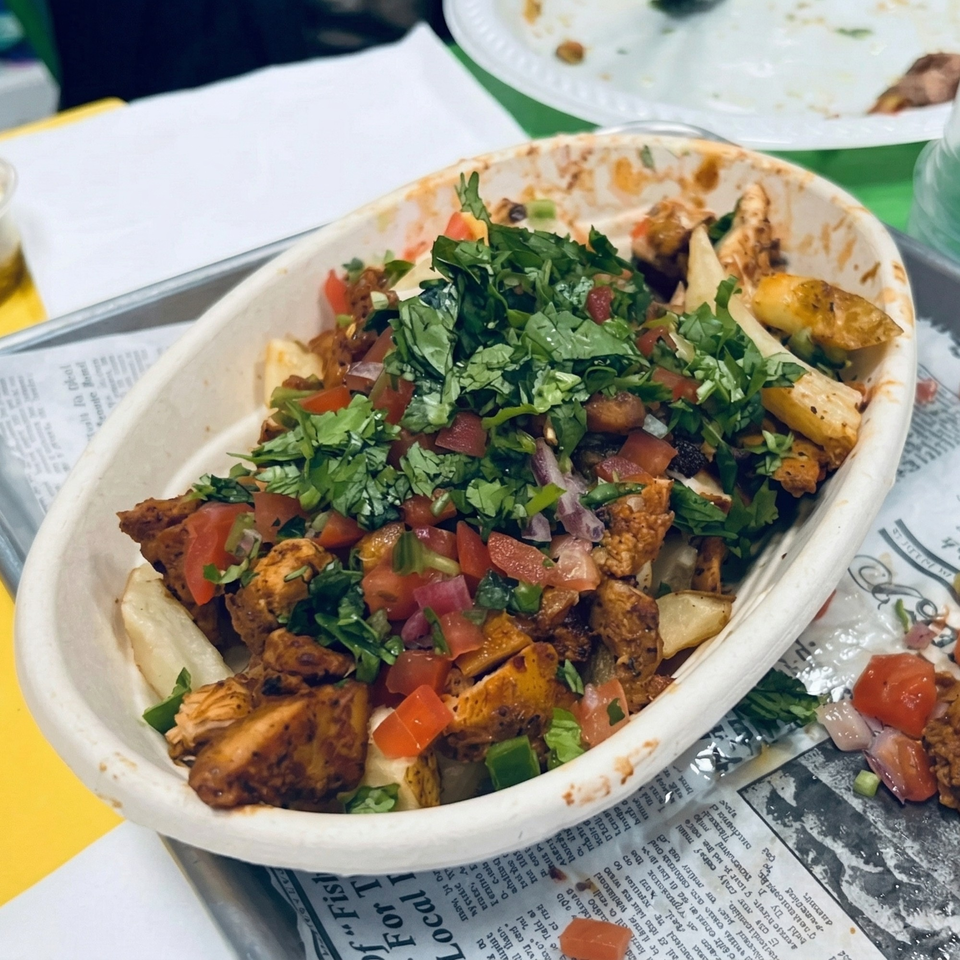 A white bowl filled with seasoned chicken, diced tomatoes, and fresh cilantro on a metal tray.