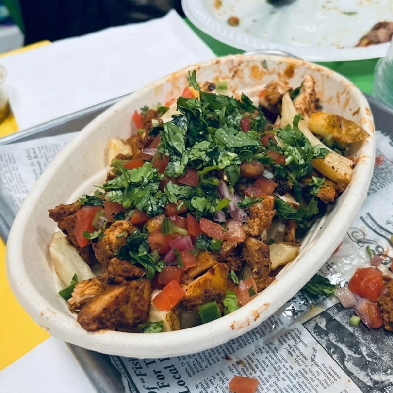 A white bowl filled with seasoned chicken, diced tomatoes, and fresh cilantro on a metal tray.