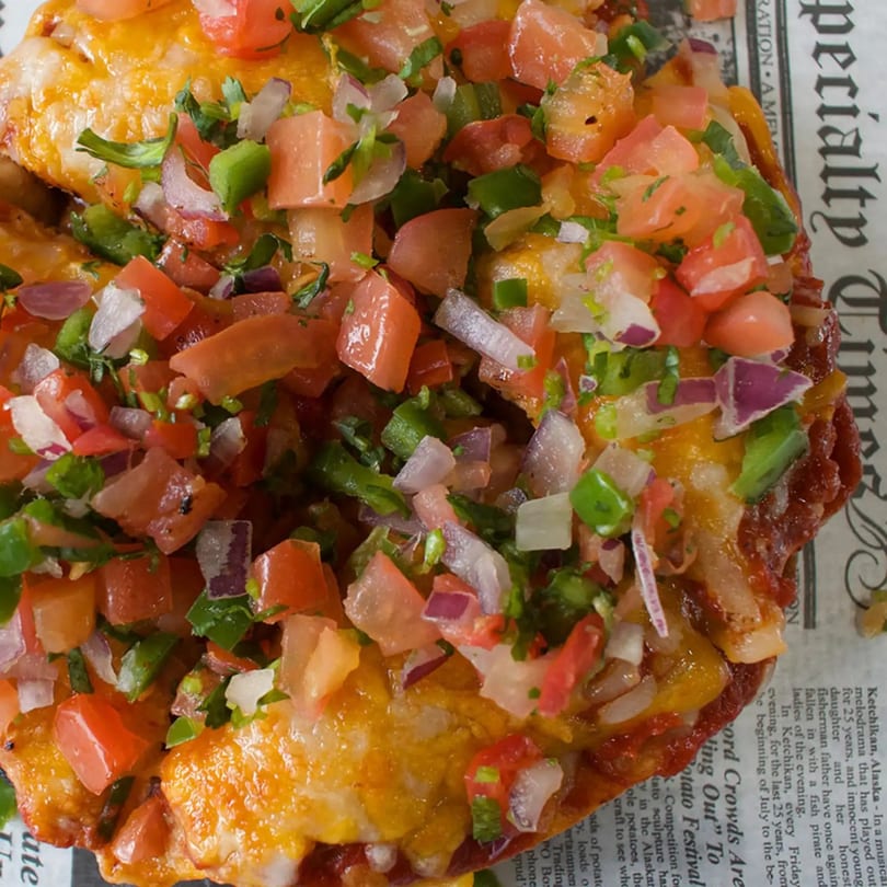 Close-up of a cheesy dish topped with fresh pico de gallo, including diced tomatoes, onions, and cilantro.